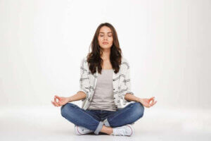 concentrated woman in casual clothes meditating with closed eyes while sitting in lotus pose on the floor