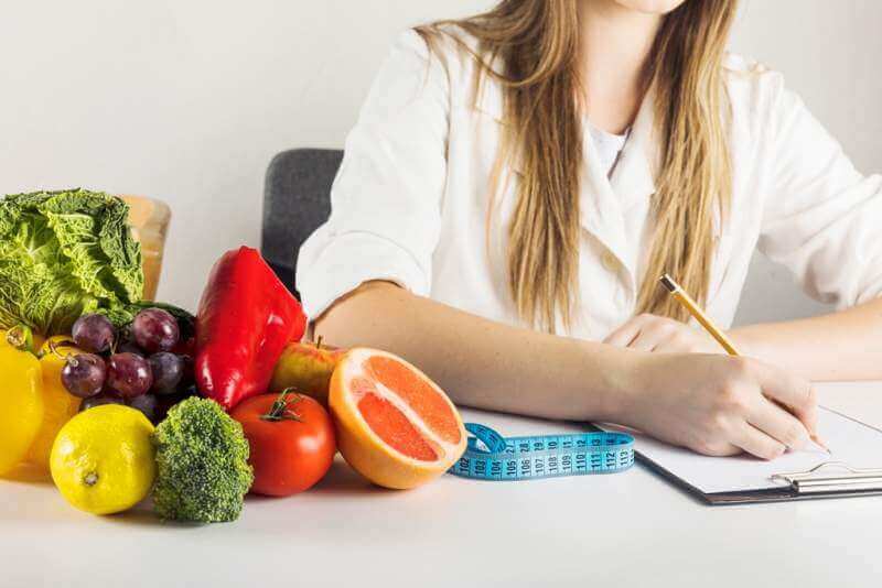 dietician-s-hand-writing-clipboard-with-healthy-food-desk