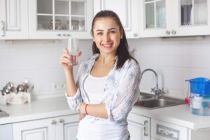 Young healthy woman drinking filtered water on the kitchen