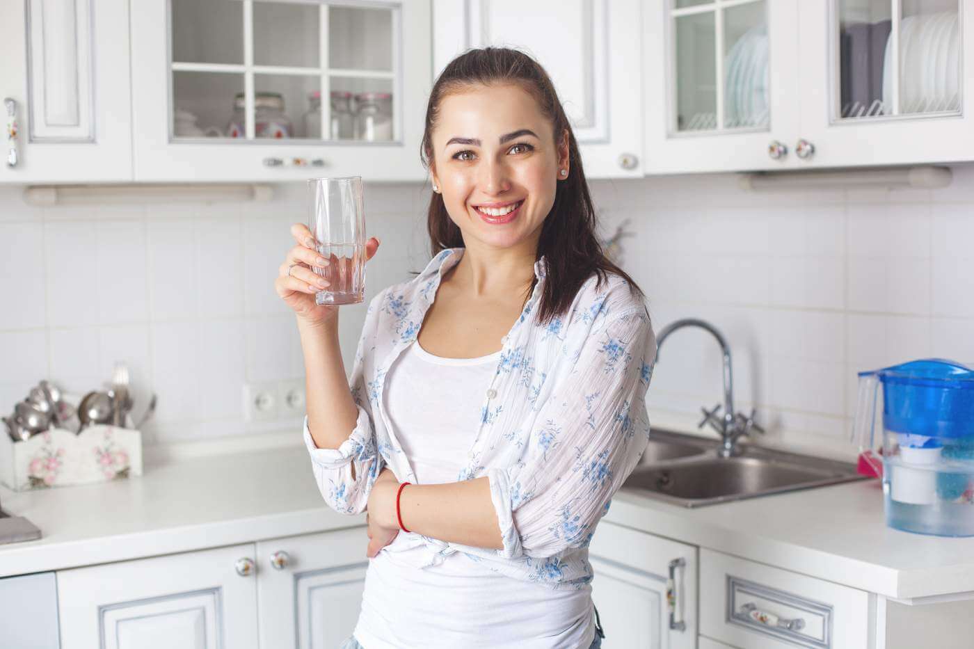 Young healthy woman drinking filtered water on the kitchen
