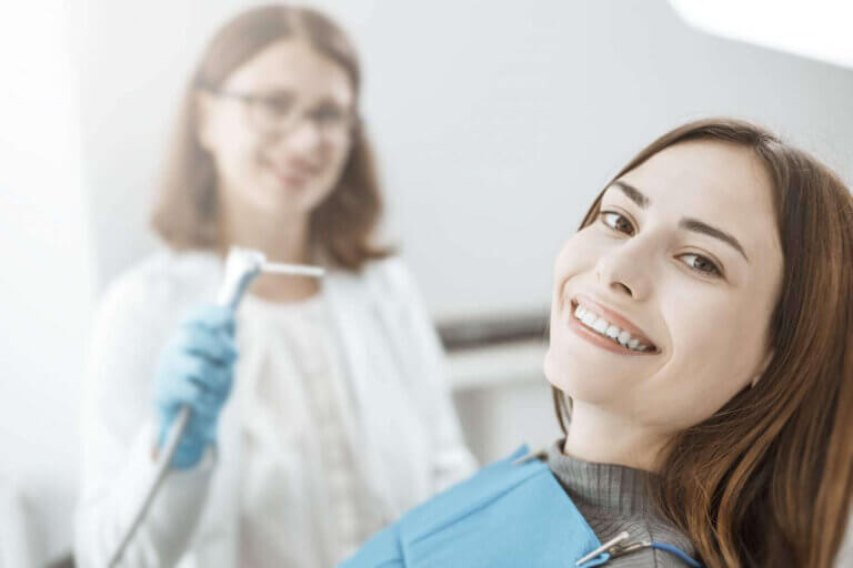 young woman sits in a dental chair and smiles with white and healthy teeth