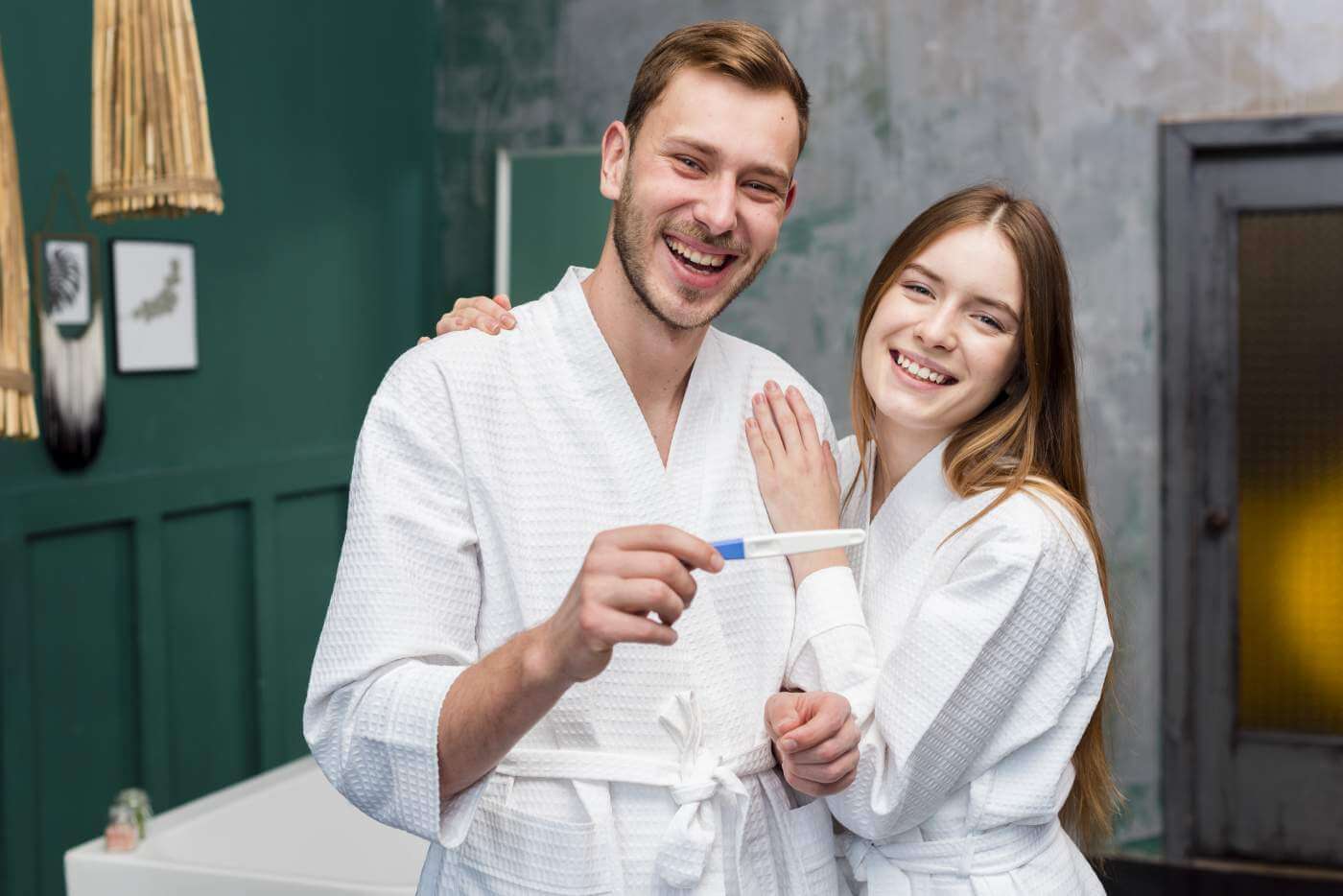 Happy couple in bathrobes holding pregnancy test