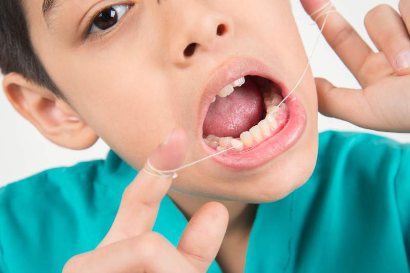 Little boy using dental floss to clean tooth