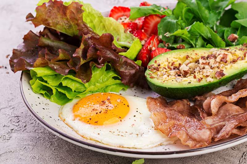 Plate with a keto diet food. fried egg, bacon, avocado, arugula and strawberries