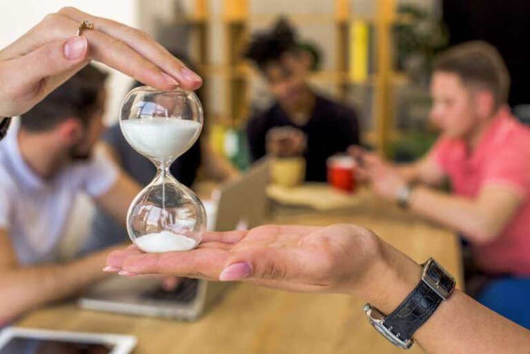 Human hand holding hourglass in front of people