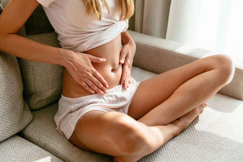 pregnant-woman-holding-hands-belly-sitting-sofa-home