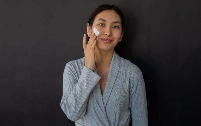 smiling-asian-woman-applying-cream-on-face