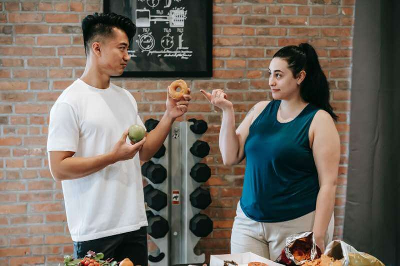 asian-instructor-with-food-and-ethnic-plump-woman-looking-at-each-other-in-gym